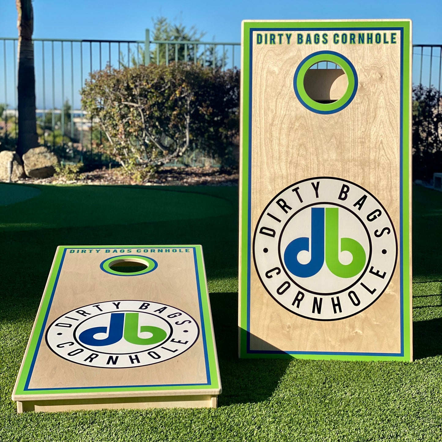 Two white cornhole boards with a 'Dirty Bags Cornhole' logo in green and blue, placed on grass.